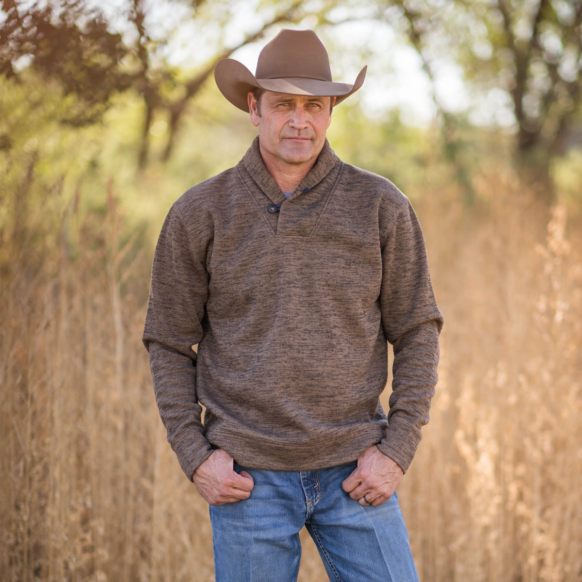 Stran T Smith wearing a tan cowboy hat, jeans and a Olathe Pullover in Heather Chocolate color in an outdoor setting.