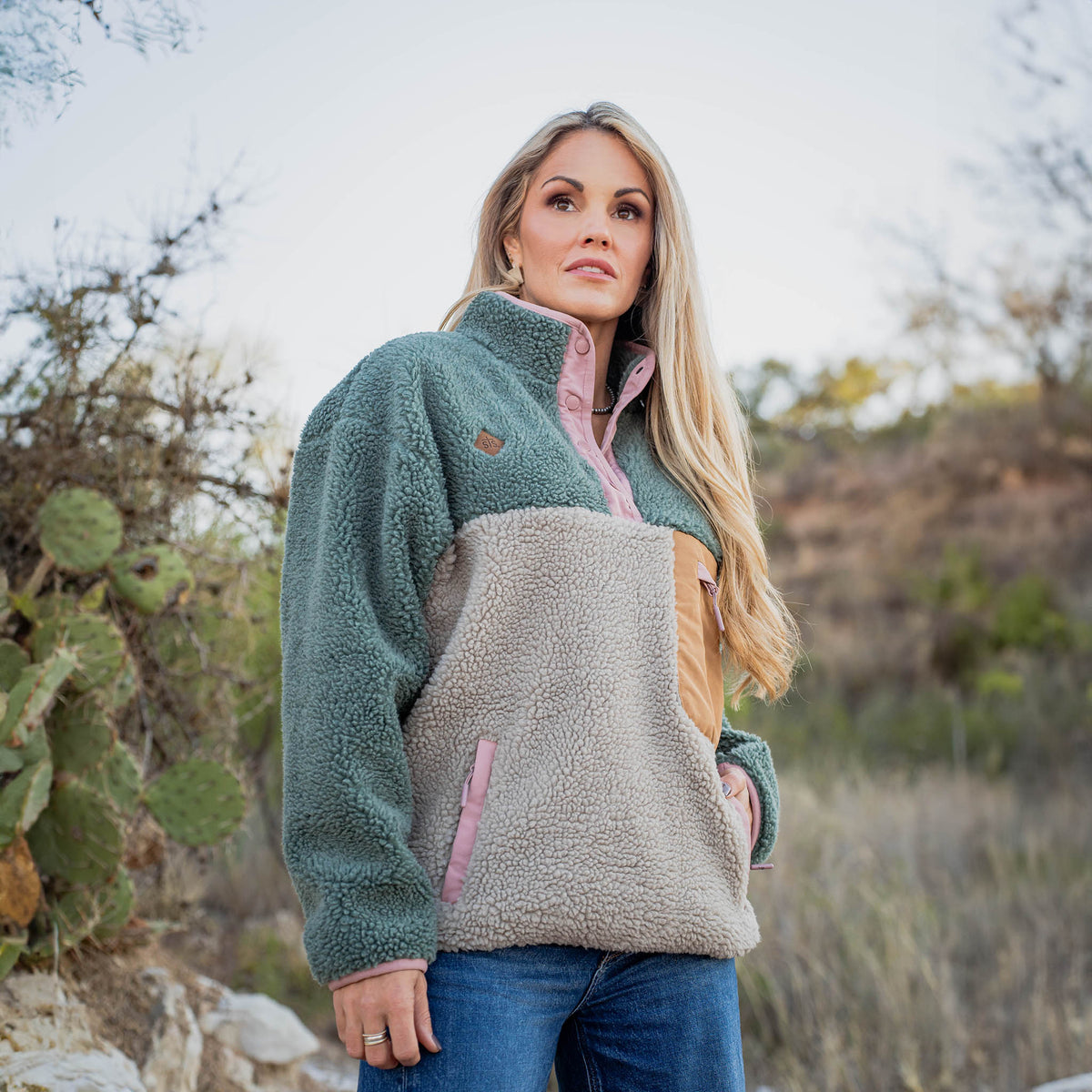 Woman wearing a two-tone fleece pullover in a natural setting with cacti and desert plants.