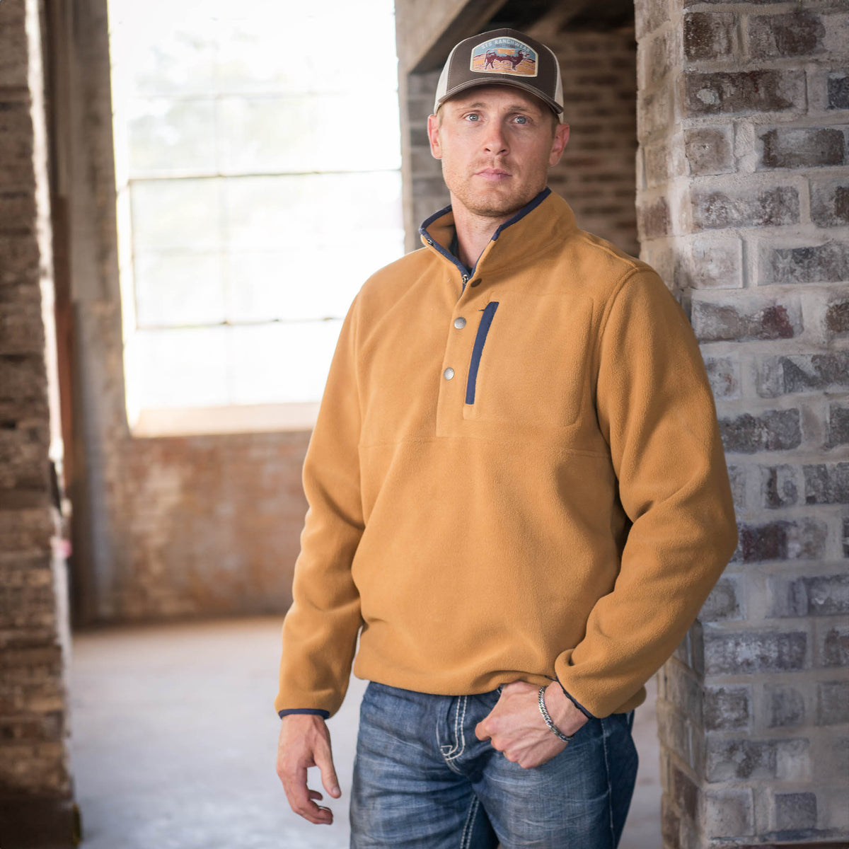 Man wearing a hat and a camel-colored pullover with a collar, four-button neck closure, and fleece-lined pockets.