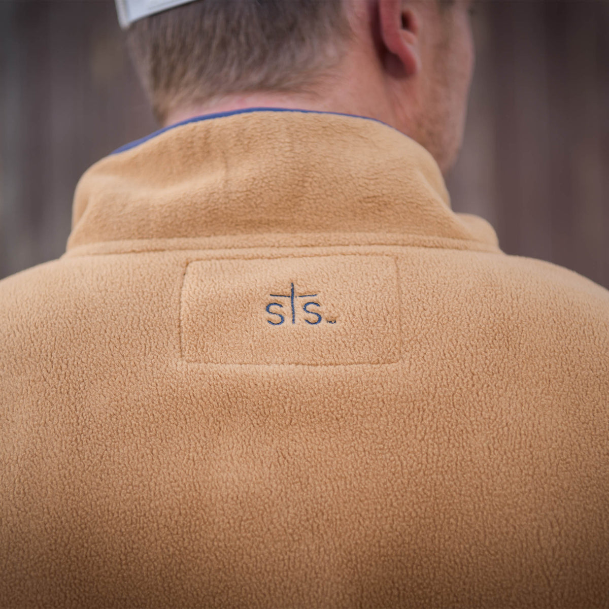 Detail of a men's camel-colored pullover with a collar and STS logo embroidery on upper back.