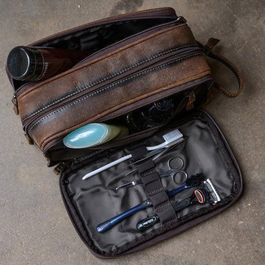side open view of toiletries in our canvas bull camo and full grain leather triple zip closure shave kit on cement ground