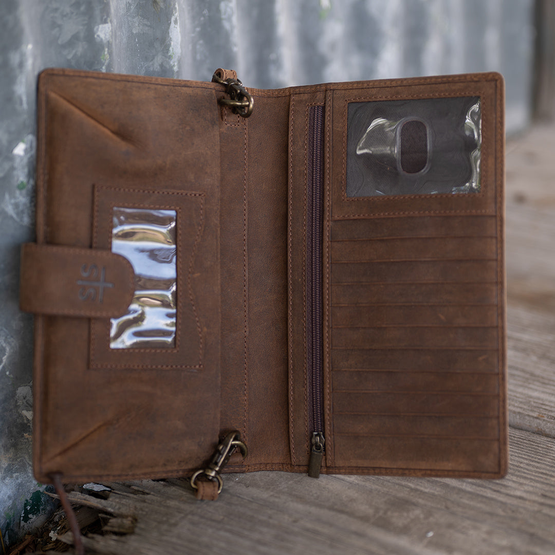 Inside a hair on hide cowhide and genuine leather wallet with 1 zip closure pocket, 2 ID slots and card slots leaning against a metal building.