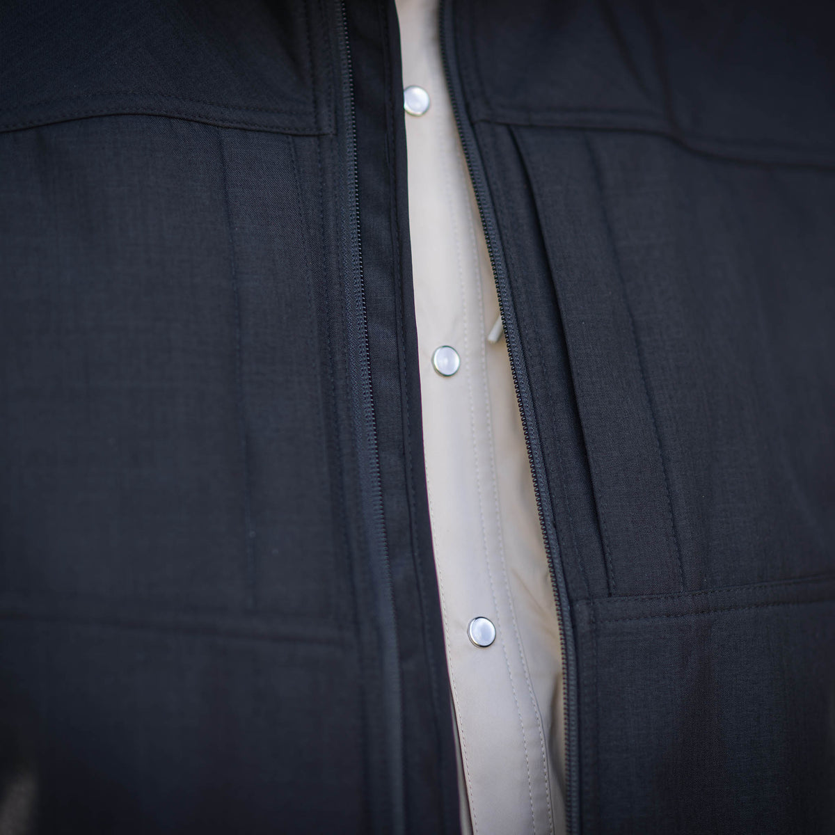 Close up of the front zipper open over a cream pearl snap shirt.