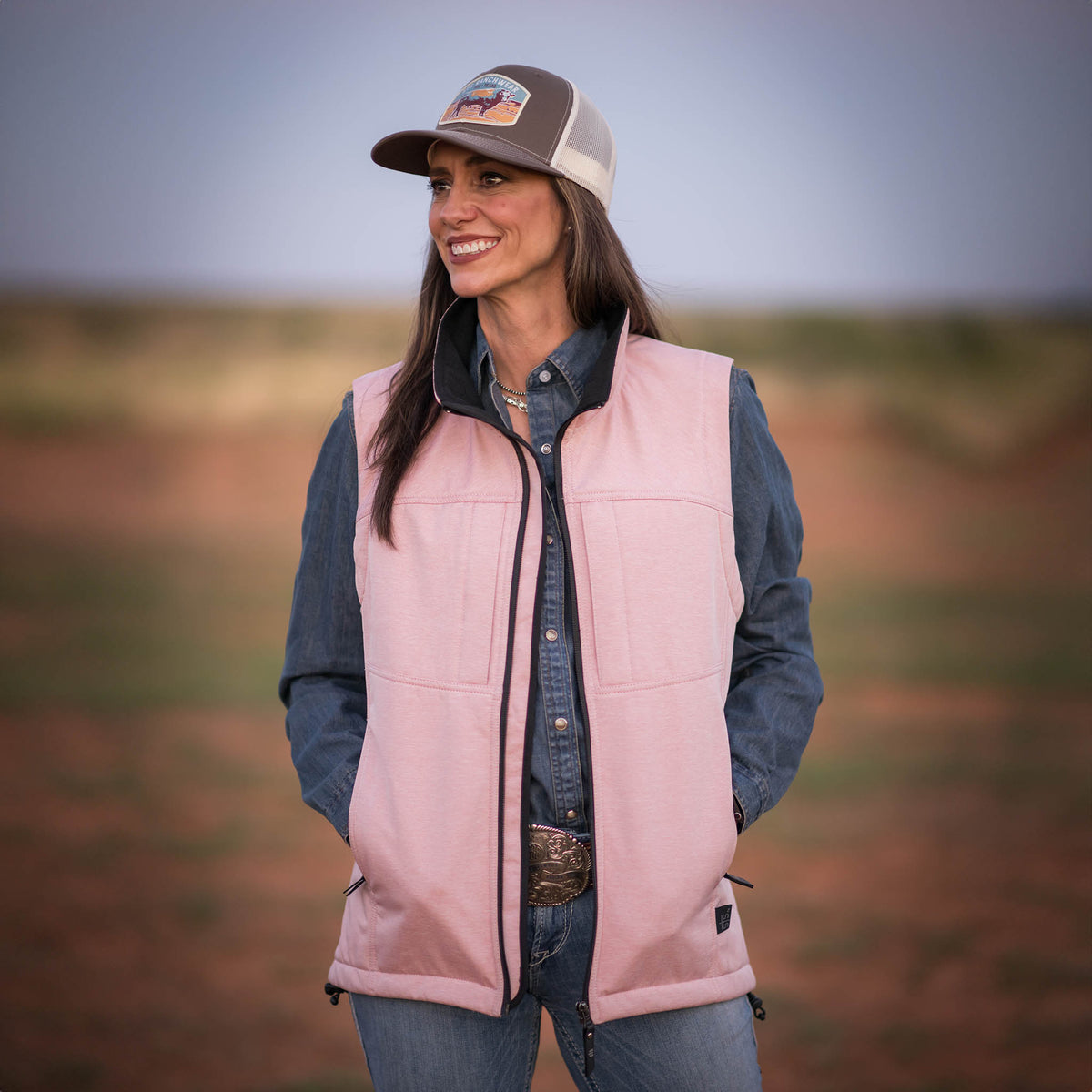 Jen Smith in an outdoor setting wearing a hat, denim long sleeve shirt, jeans and a pick softshell vest.