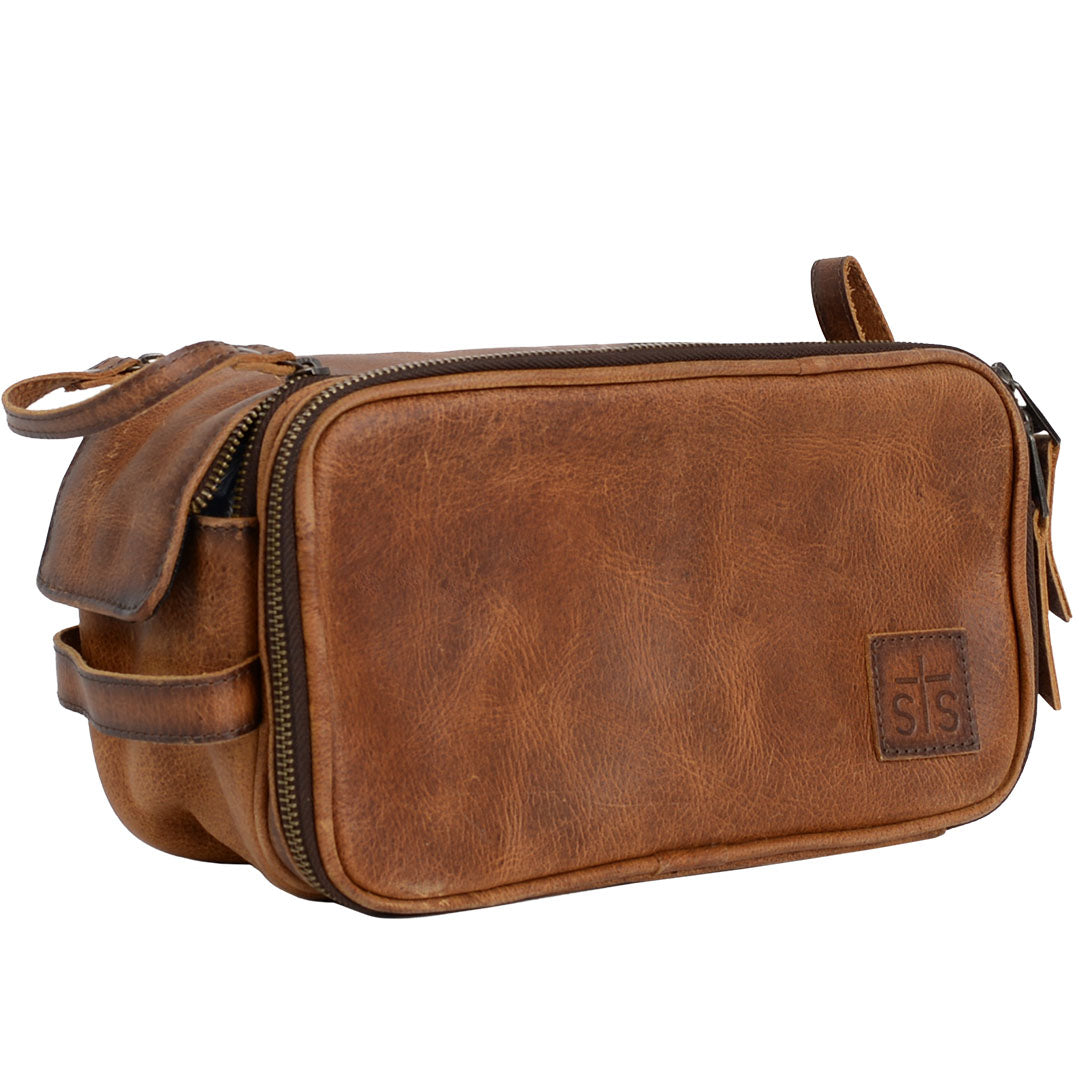 A brown genuine leather shave kit with dual top zip closure, leather carrying handle and brown leather patch with STS embossed on a white background.