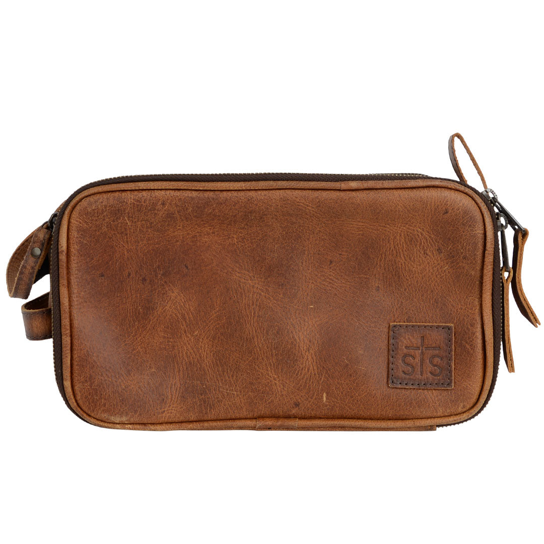 A brown genuine leather shave kit with dual top zip closure, leather carrying handle and brown leather patch with STS embossed on a white background.