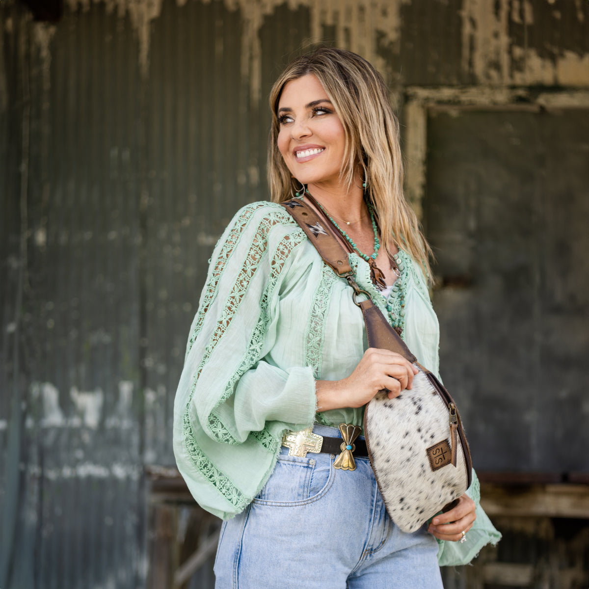 Woman wearing green shirt and jeans with a cowhide belt bag across her body.