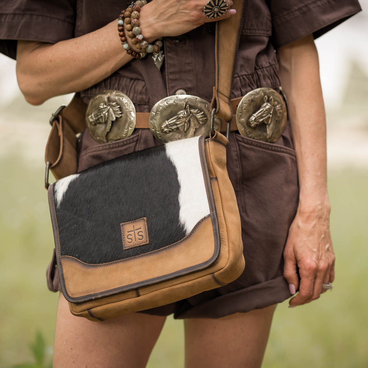 Person holding a crossbody bag with leather and cowhide accents, wearing a brown outfit.