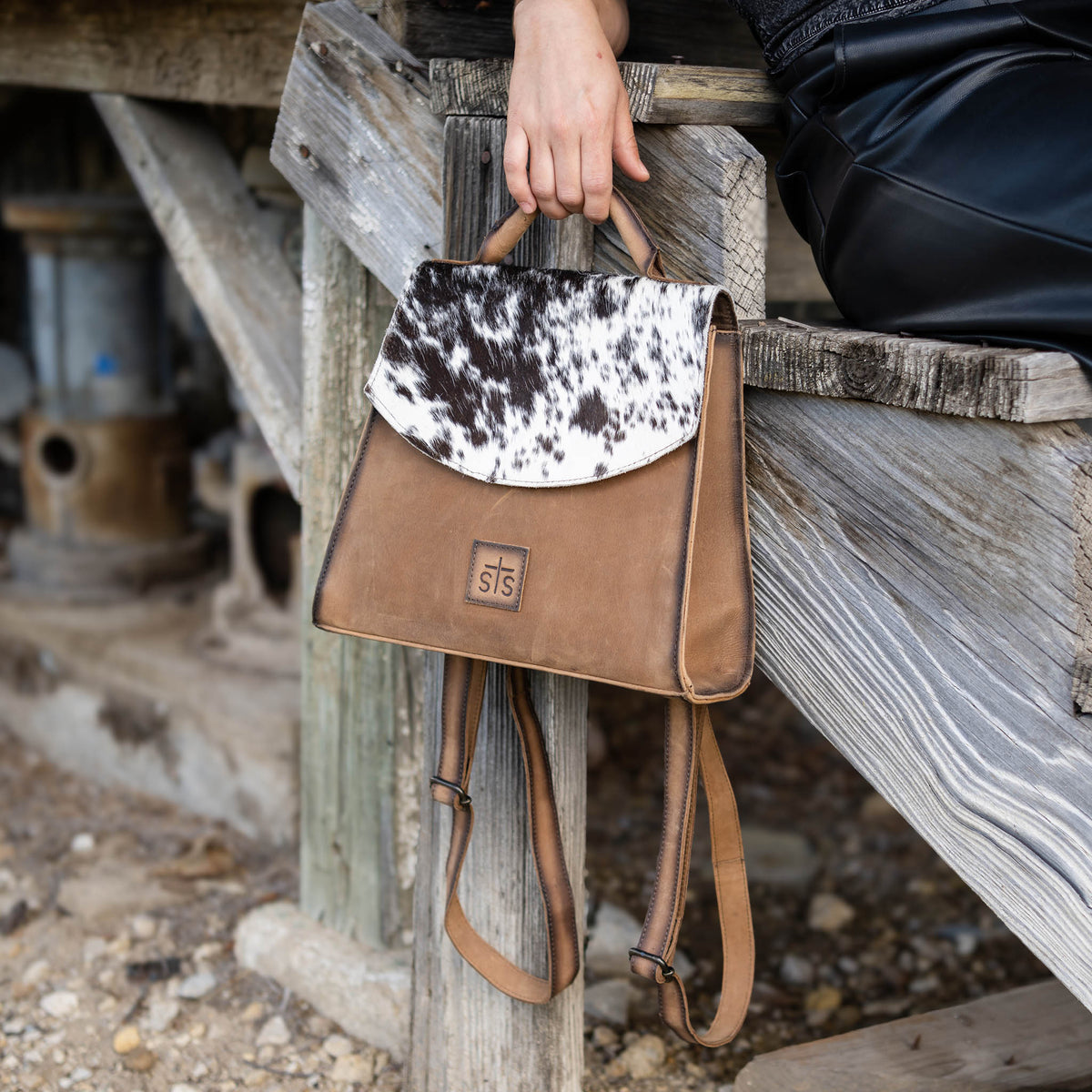 Person holding a brown genuine leather backpack with black and white hair on hide accents.