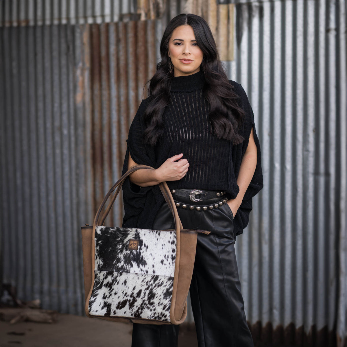 Woman holding a genuine leather tote bag with black and white hair on hide cowhide accents and dual rolled leather handles.