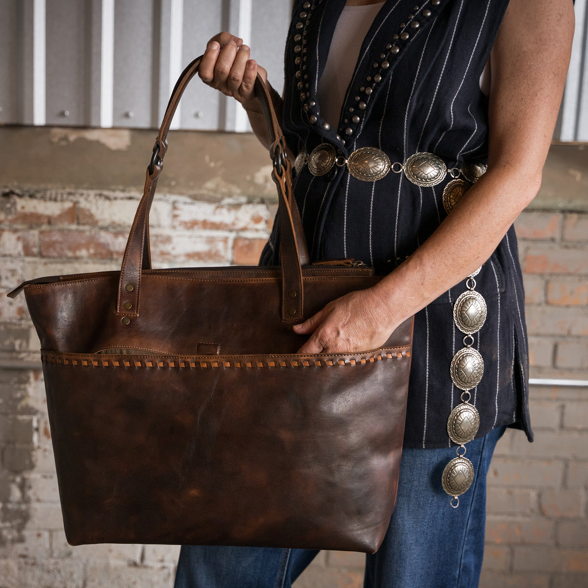 Tiffany Cooper with her hand inside the back slip pocket of our Bandera chocolate leather tote purse with buckstitch, top zip closure and magnetic buckle front pocket