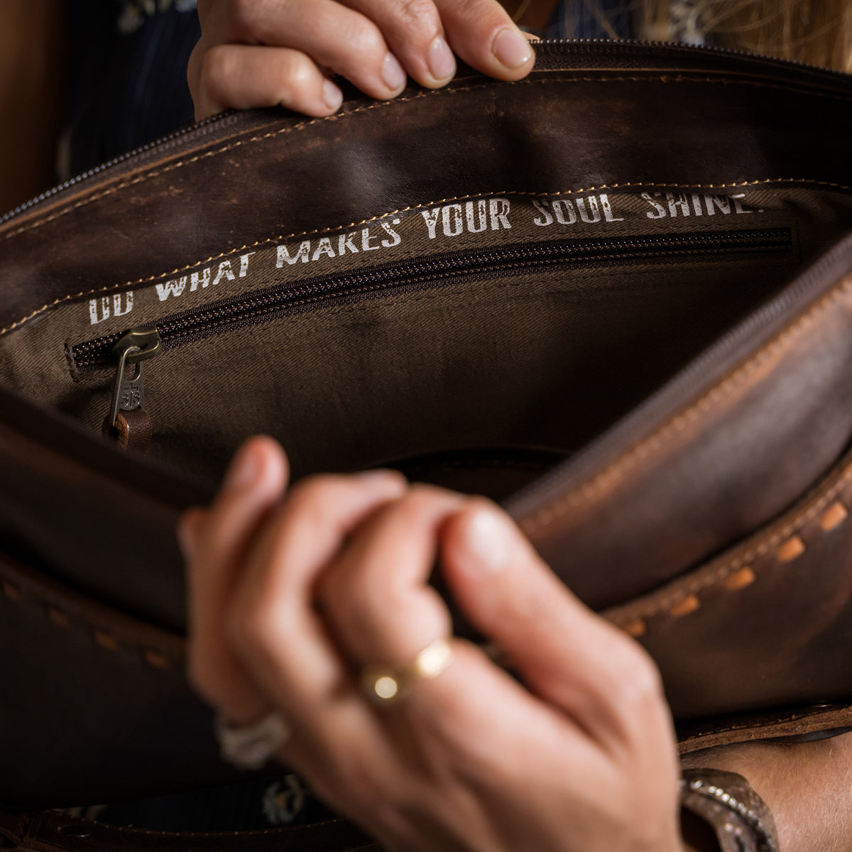 closeup of a woman's hands holding open our Bandera chocolate leather shoulder bag with buckstitch, top zip closure, front magnetic pocket and back slip pocket