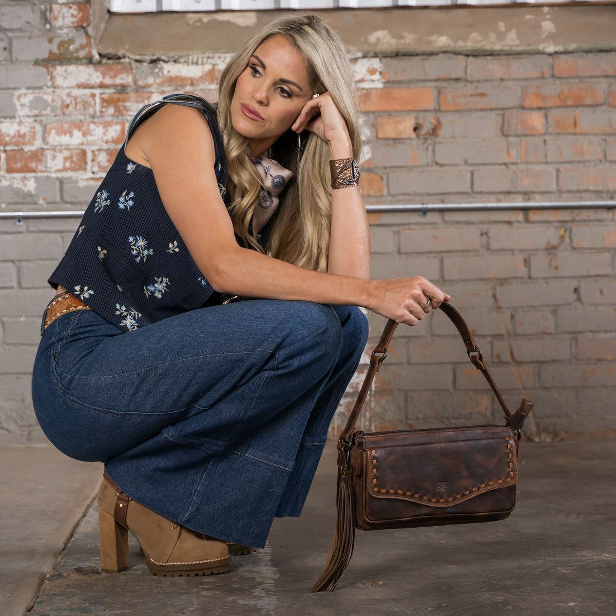 Terryn cooper holding our Bandera chocolate leather shoulder bag with buckstitch, top zip closure, front magnetic pocket and back slip pocket