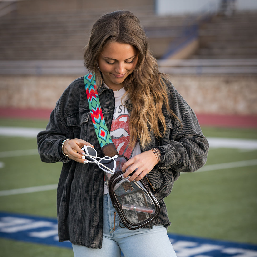 Woman holding sunglasses and a small bag on a sports field.