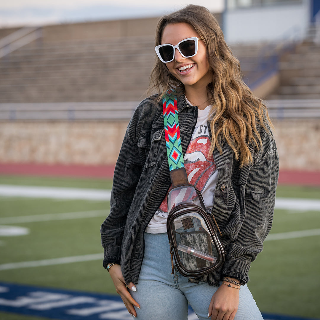 Woman with sunglasses and a colorful bag on a sports field.