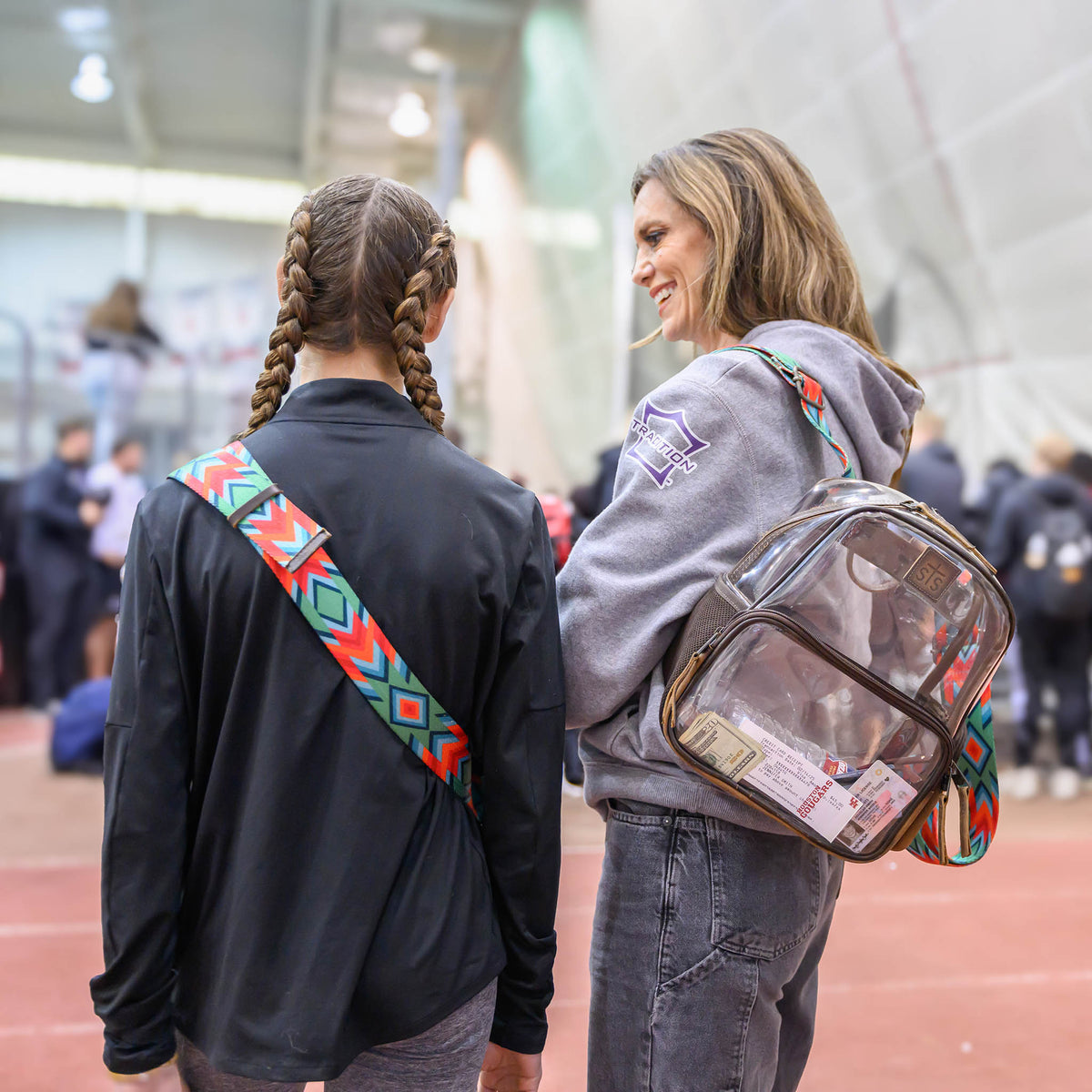 Two women walking on a track or field, one with a clear a clear backpack.