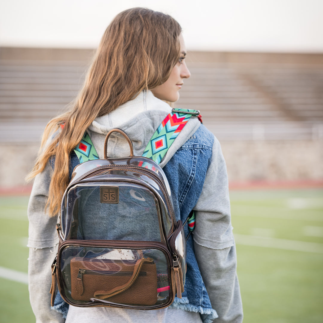 Person wearing a transparent backpack with brown leather accents on a sports field.