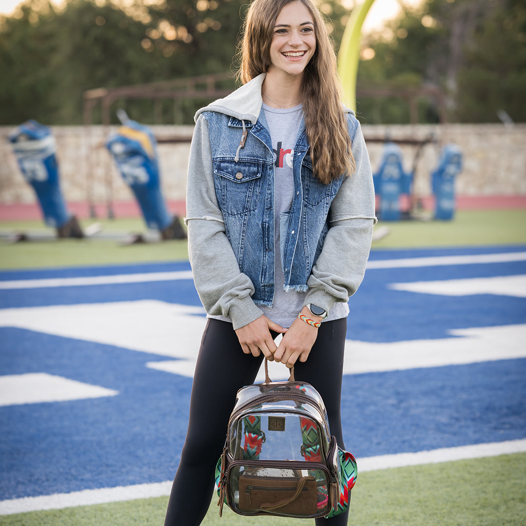 Woman holding a clear backpack on a football field.