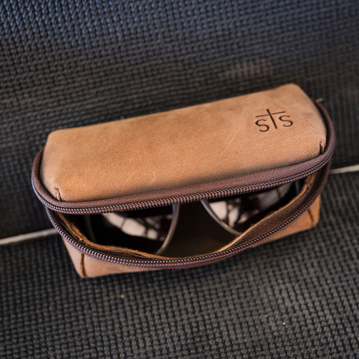 Brown zippered sunglasses case with 'sts' logo.