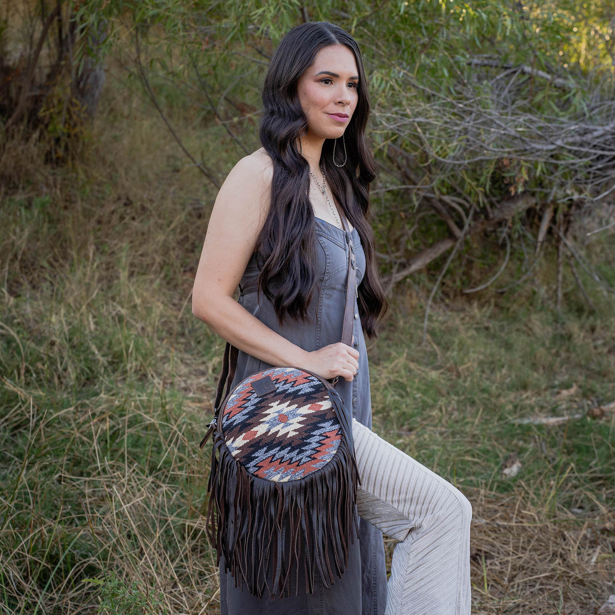 Woman holding a colorful fringed bag in a natural setting.