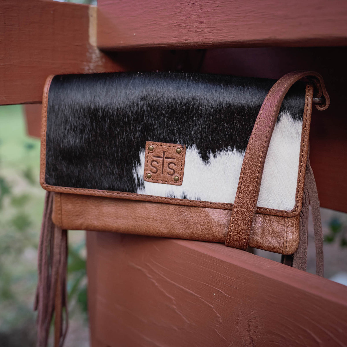 Handbag with black, white, and brown cowhide accents on a wooden surface.