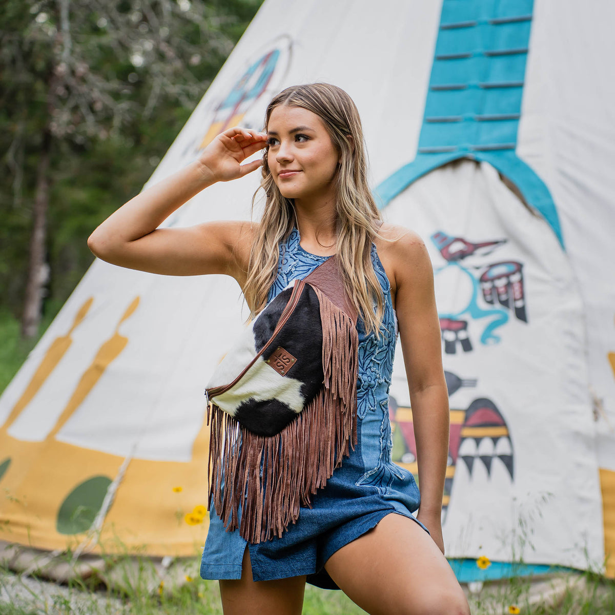 Woman posing in front of a colorful teepee with a fringed belt bag across her body.