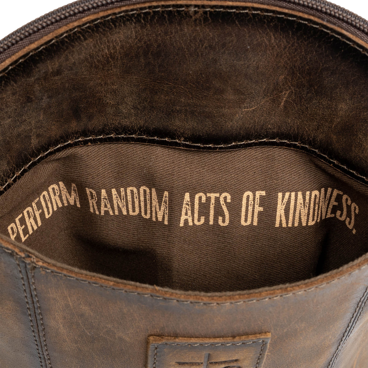 "Perform random acts of kindness." gold letters printed in the lining of a leather crossbody purse on a white background.