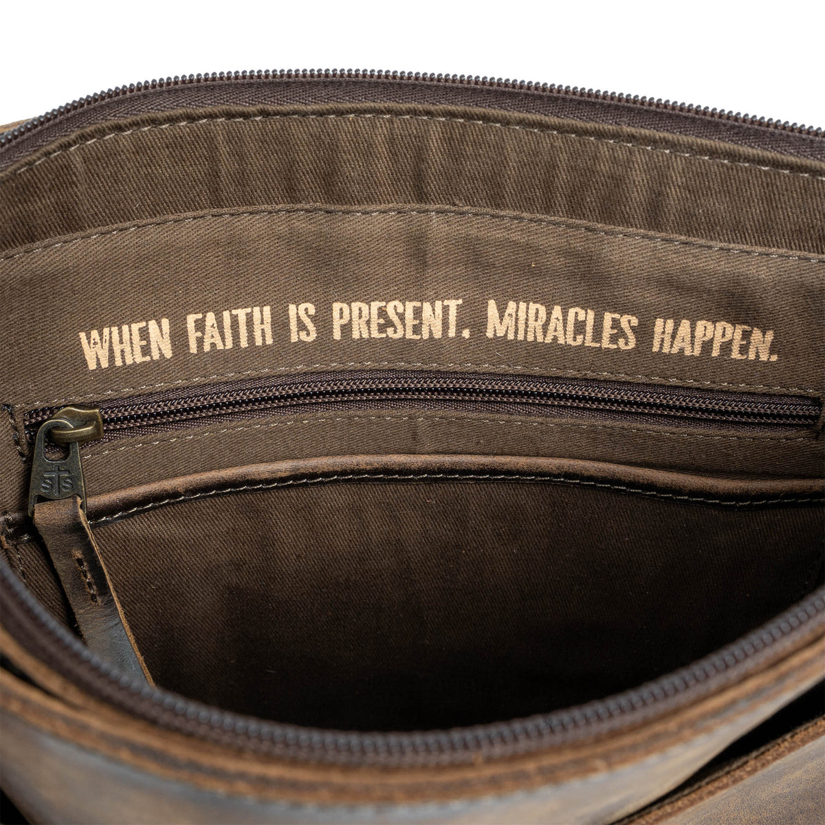 "When faith is present. Miracles happen." gold letters printed in the lining of a leather purse on a white background.