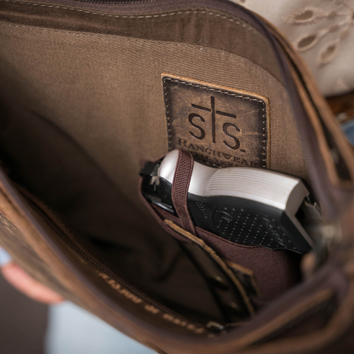 Close up view of a weapon in the conceal carry compartment in a leather crossbody purse.