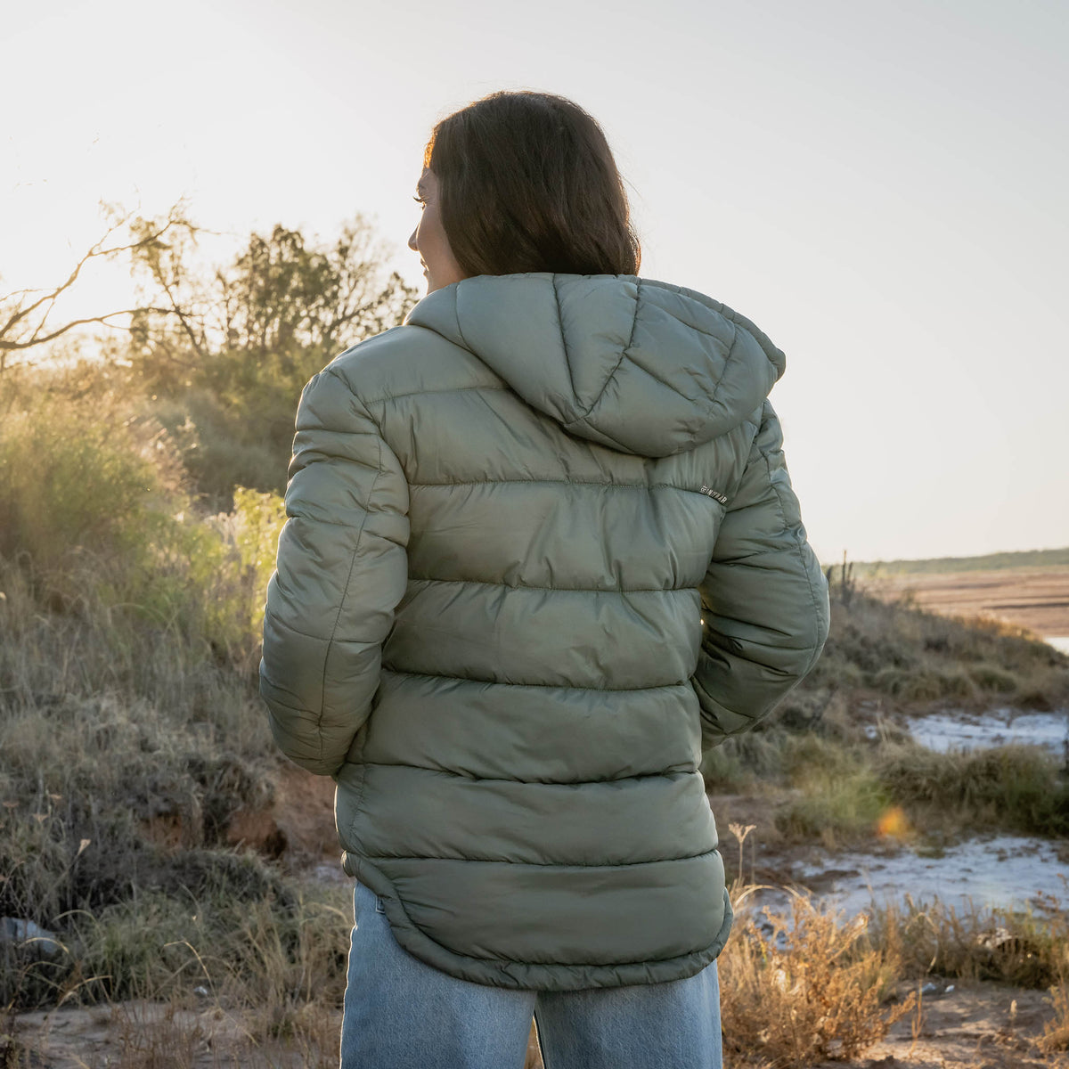 Person wearing a green puffer jacket standing in a natural landscape.