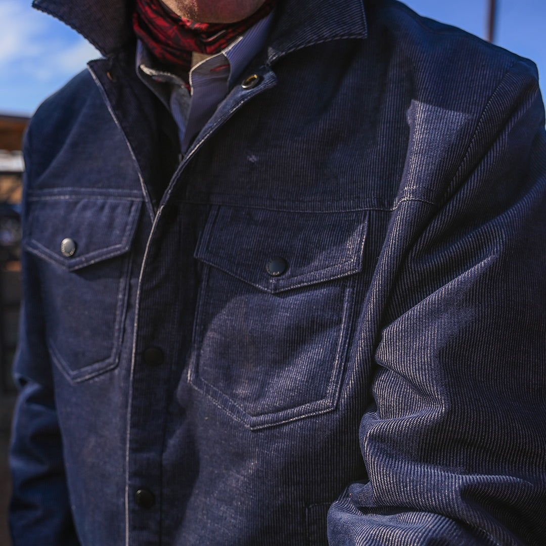Close up of a long-sleeved blue corduroy jacket with snap front closure and two chest pockets.