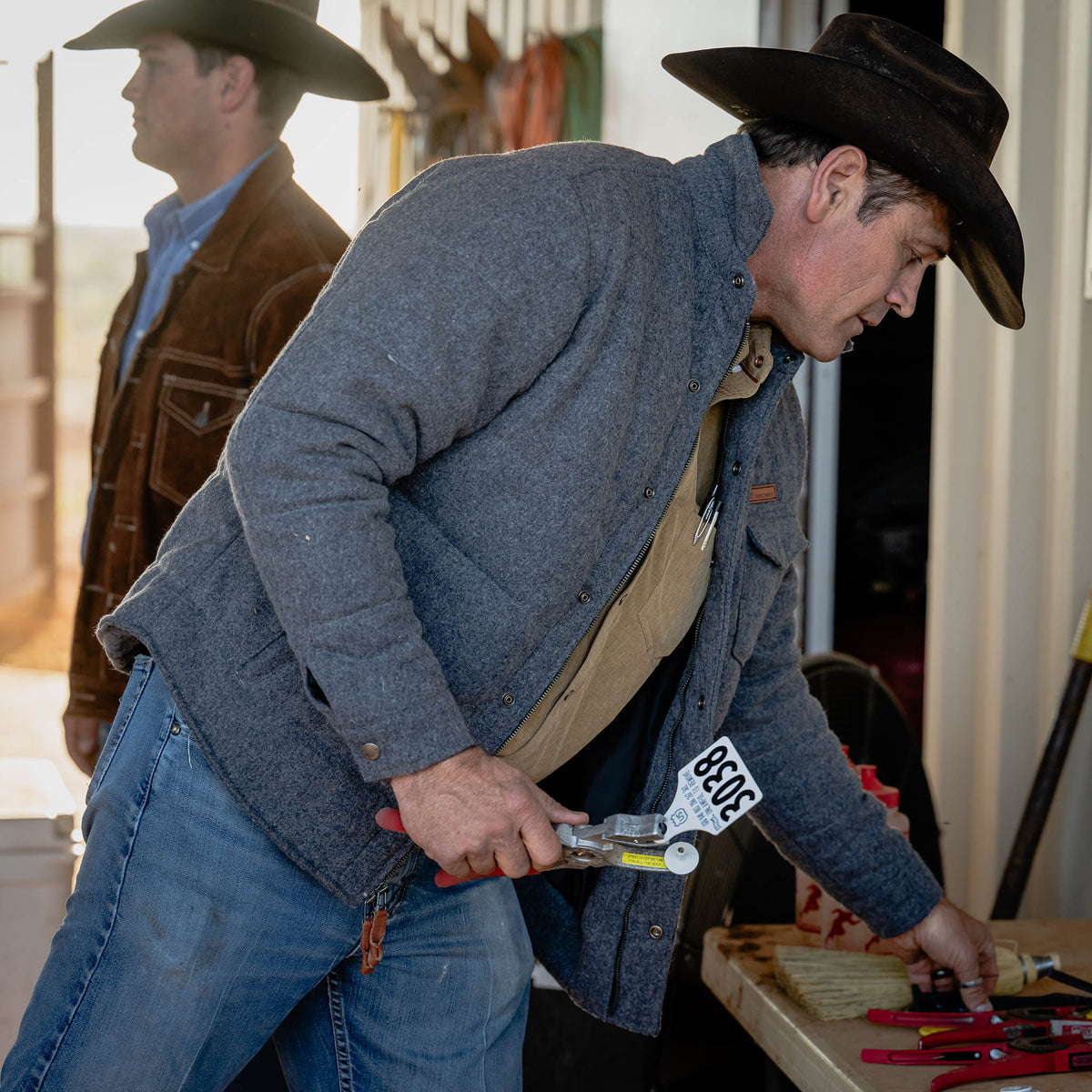 Man in cowboy hat and coat holding a wrench with a visible 'Rodeo' tag, standing in a room.