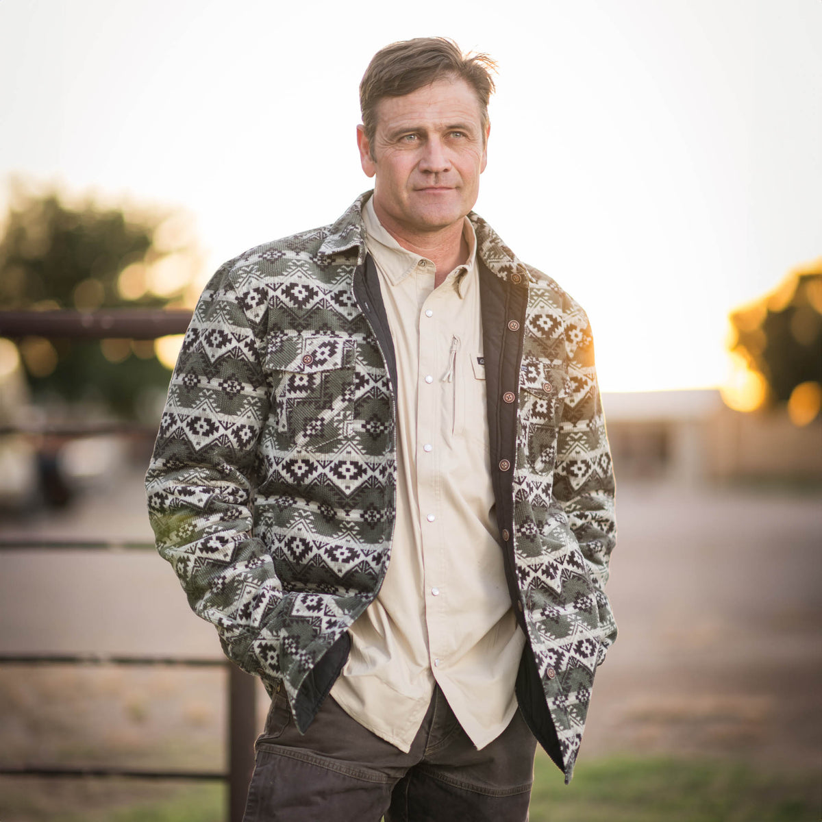Stran T Smith in an outdoor setting wearing a reversible jacket with a geometric pattern in green, beige, and black colors, featuring button front closure and multiple pockets.