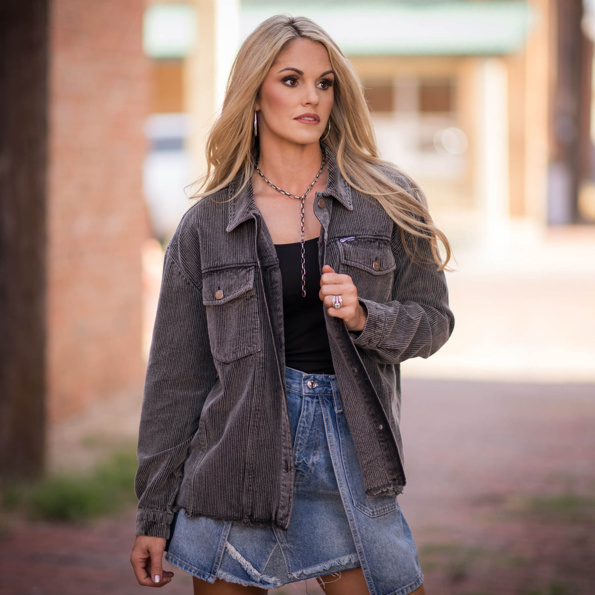 Woman in an outdoor setting wearing a gray women's corduroy shacket with button closures, chest pockets, button cuffs, and frayed waist accents.