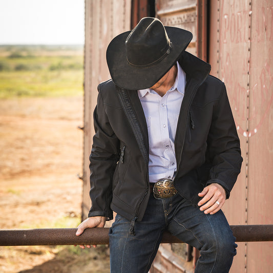 closeup of a man sitting on a railing on sts ranch wearing a black jacket with front chest zip pocket, front zip closure and hand warming pockets
