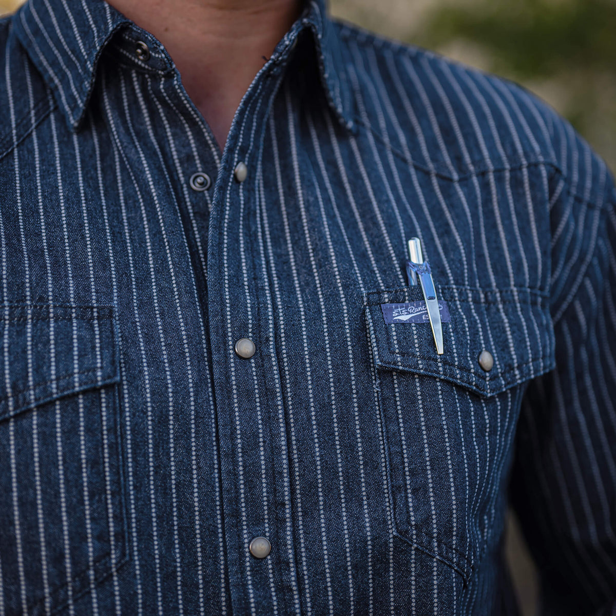 Detail of a striped men's denim button-down shirt with pearl snap closures and two chest pockets.