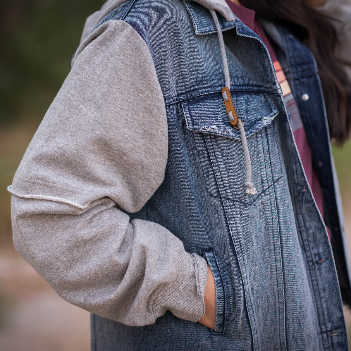 Person wearing a women's Cassie Jo denim jacket with gray sweatshirt sleeves and a drawstring hood.