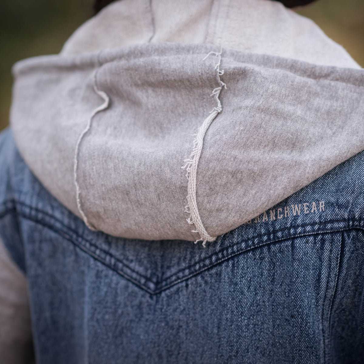 Person wearing a women's Cassie Jo denim jacket with gray sweatshirt sleeves and a drawstring hood.