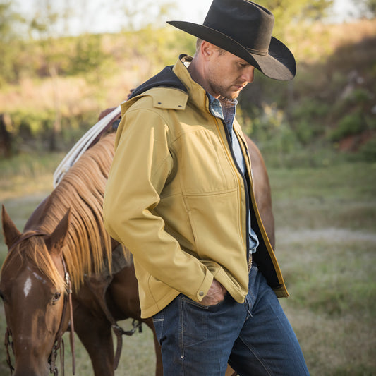 Clif Cooper wearing our curry yellow jacket with zip closure, removable hood and hand warming pockets outside in front of a brown horse