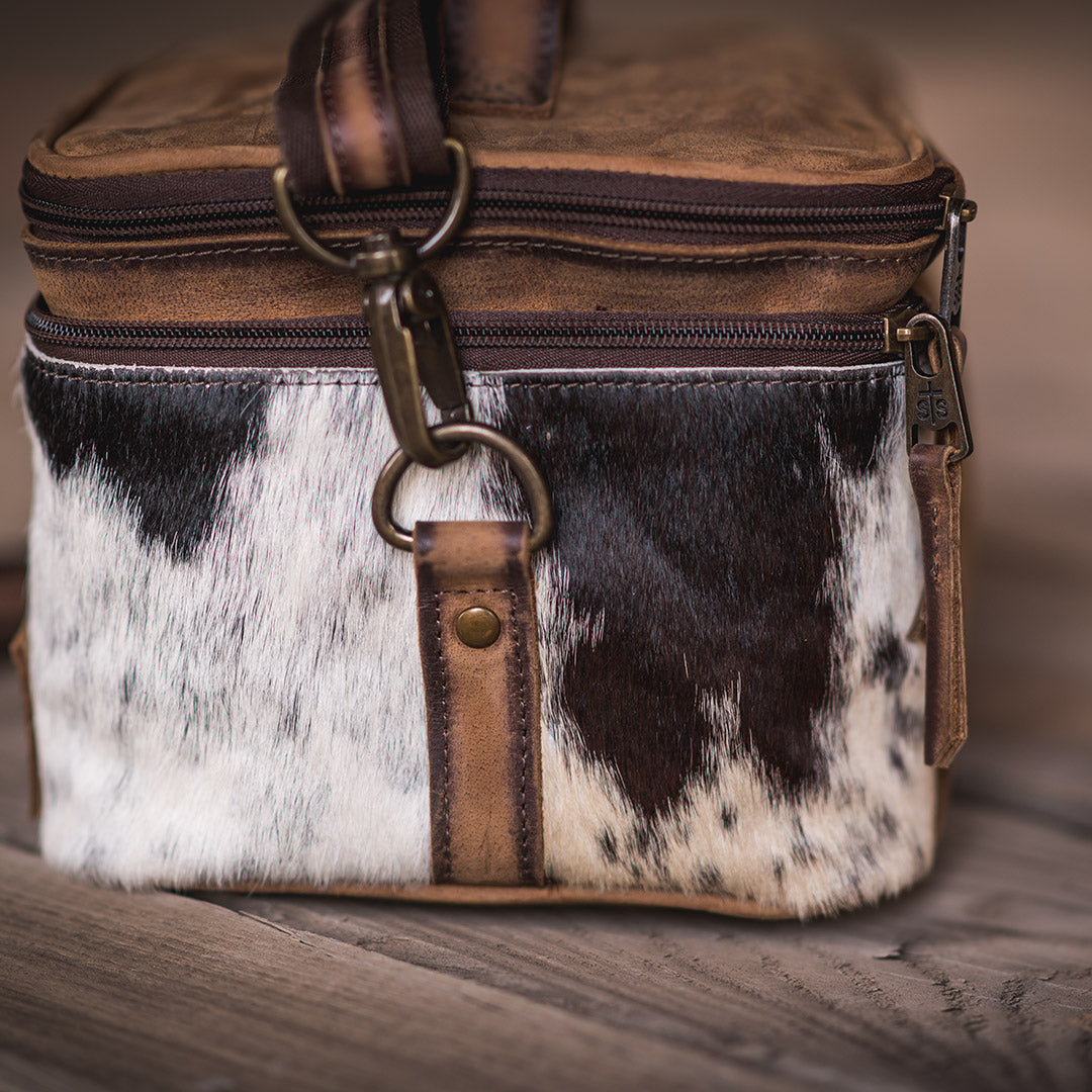 Brown and black hair on hide cowhide patterned cosmetic bag with genuine leather top, leather carrying handle and removable nylon shoulder strap.