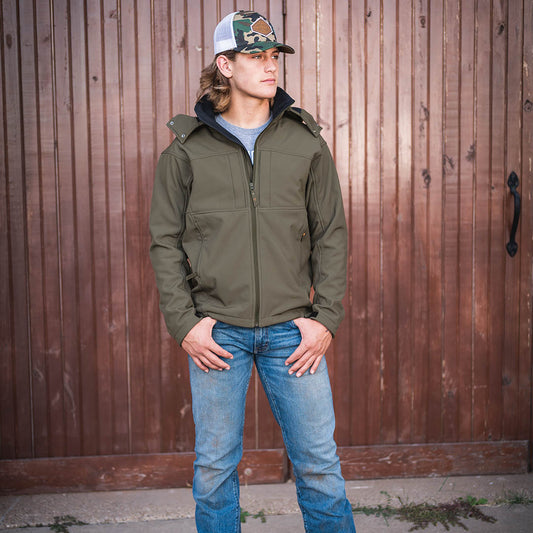 scout smith wearing our softshell olive green front zip closure jacket with removable hood in front of wooden door