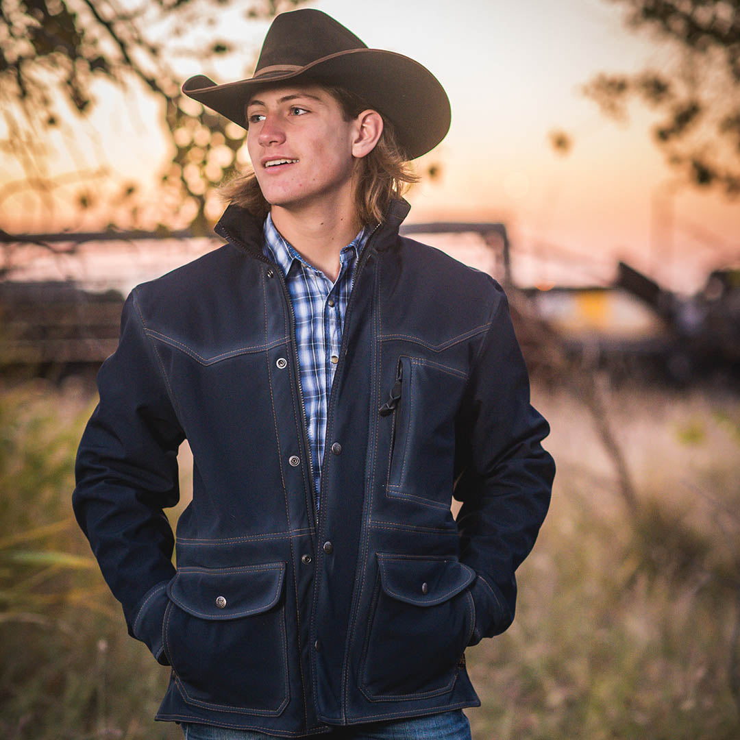 Man wearing a tan cowboy hat and navy softshell jacket in an outdoor setting.