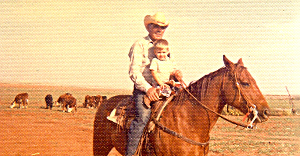 Stran T Smith sitting on top of a horse with his granddad with cows behind them.