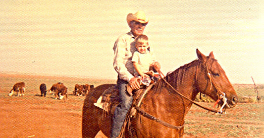 Stran T Smith sitting on top of a horse with his granddad with cows behind them.