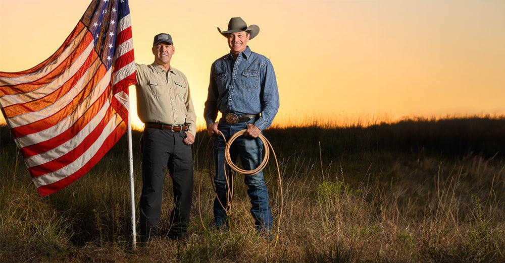 Stran T Smith and Colonel J. Craig Flowers standing in a field holding an American flag with the sun setting behind them.