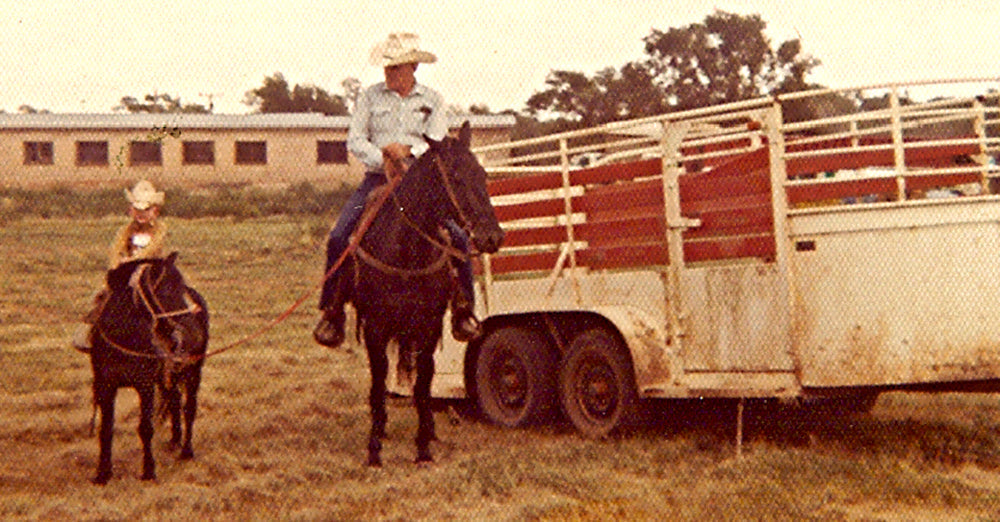 Stran T Smith sitting on a pony next to his granddad riding a horse in front of a white horse trailer.