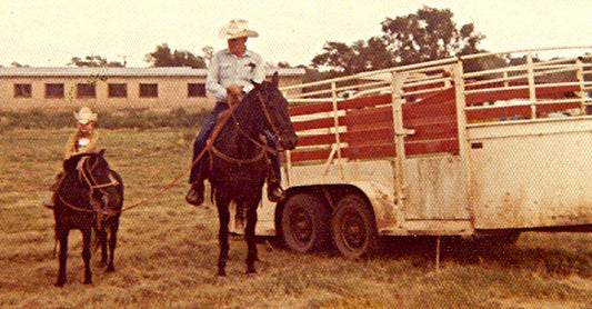 Stran T Smith sitting on a pony next to his granddad riding a horse in front of a white horse trailer.