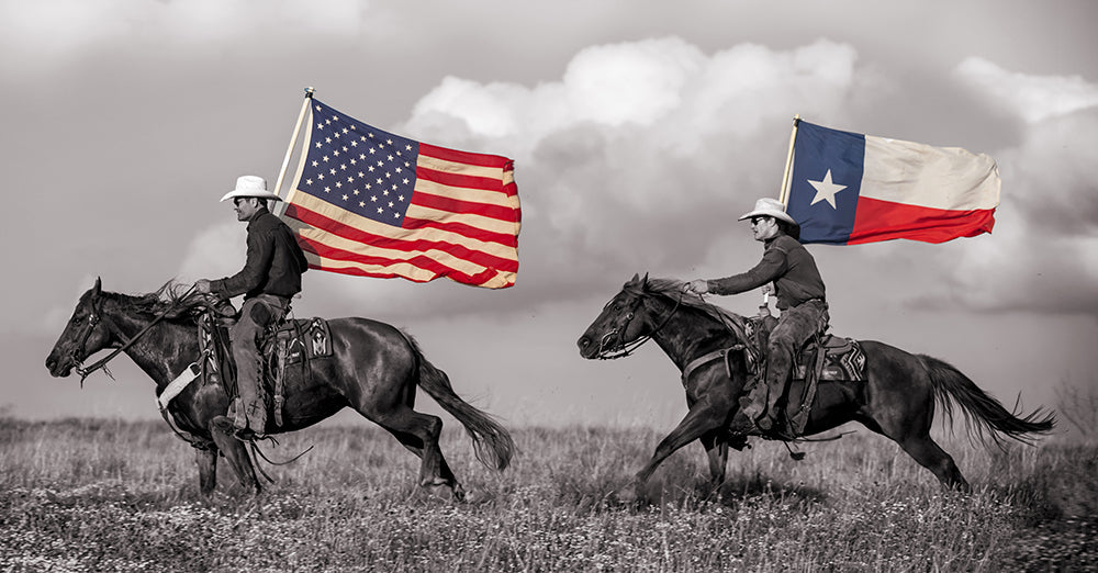 Two men wearing cowboy hats riding horses across a pasture carrying a United States flag and Texas state flag.