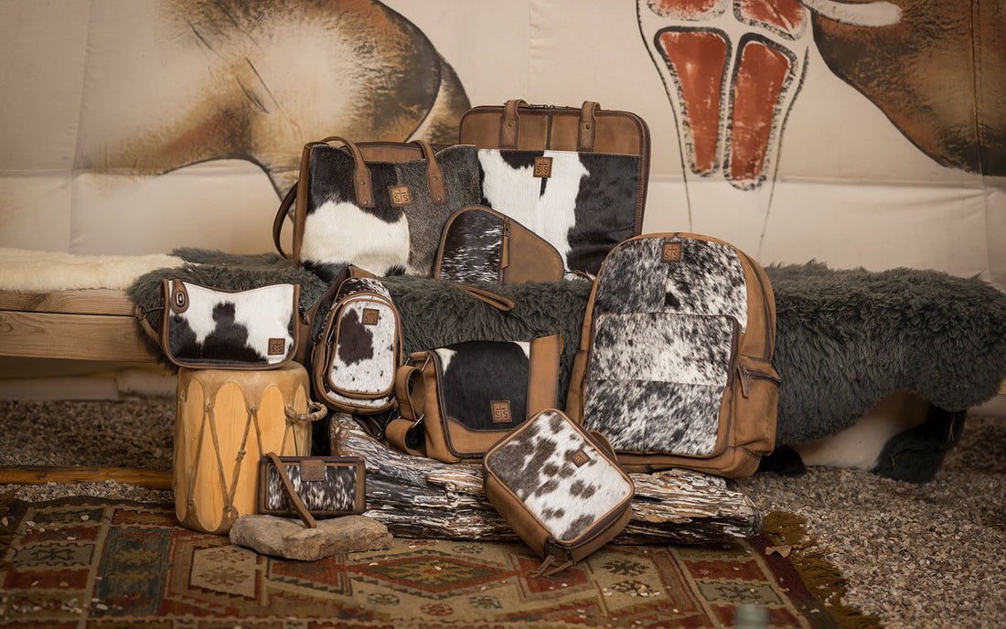 Different hair on hide cowhide handbags, wallets and backpacks stacked together on the floor.