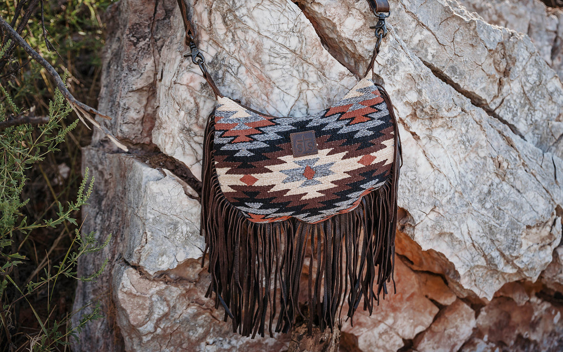 Brown, cream and gray hand woven shoulder bag with leather fringe hanging from a rock.